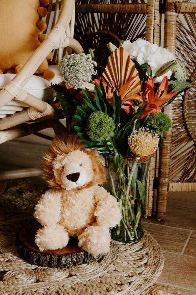 a teddy bear sitting next to a vase with flowers in it on a rug near a wicker chair