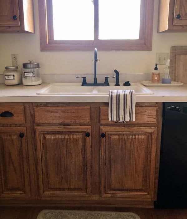 a kitchen sink and dishwasher in a small room with wooden cabinets, black appliances and a window