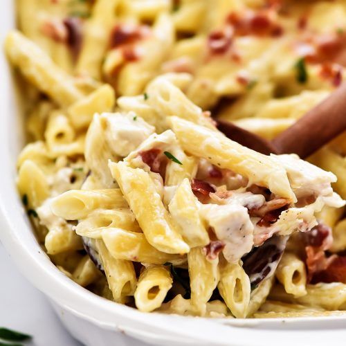 a white bowl filled with pasta and meats on top of a table next to a wooden spoon