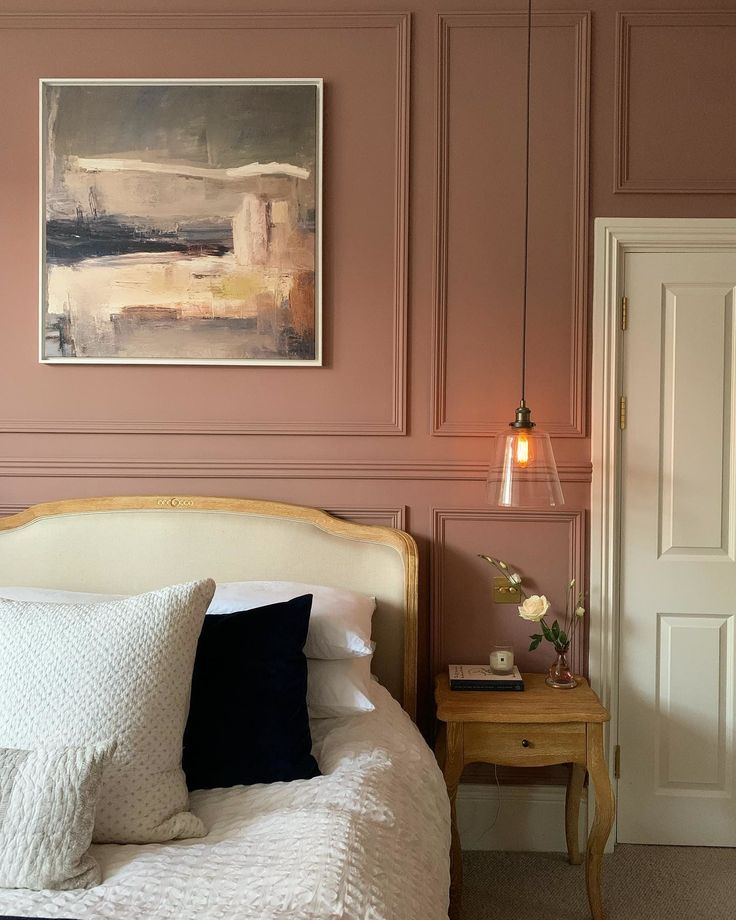 a bedroom with pink walls, white bedding and a painting hanging above the bed