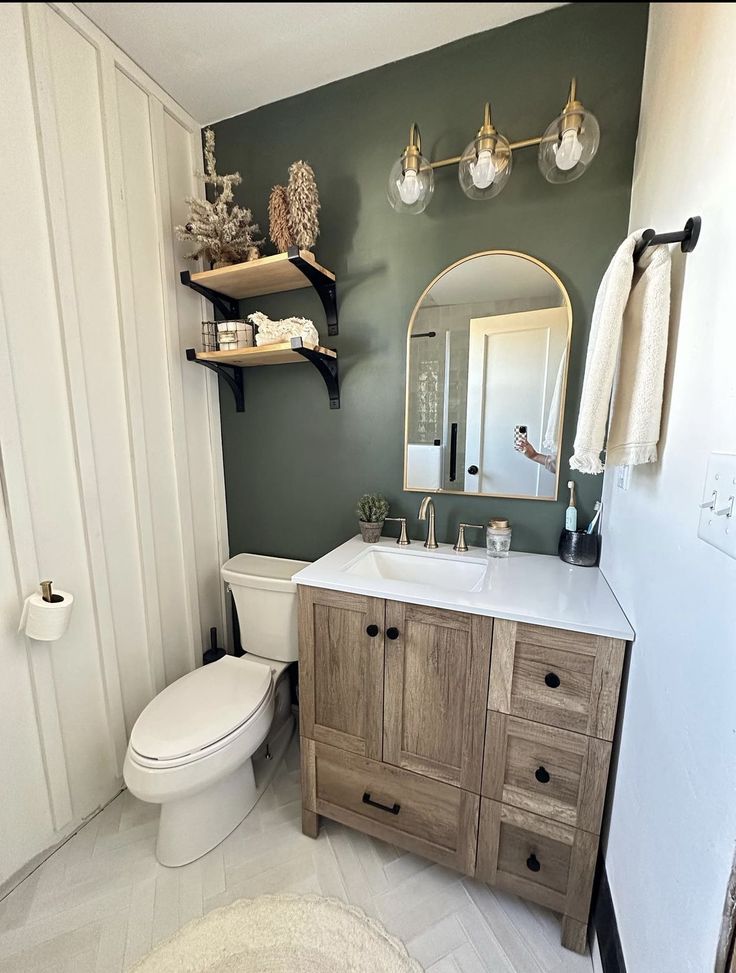 a white toilet sitting next to a wooden cabinet in a bathroom under a mirror and lights