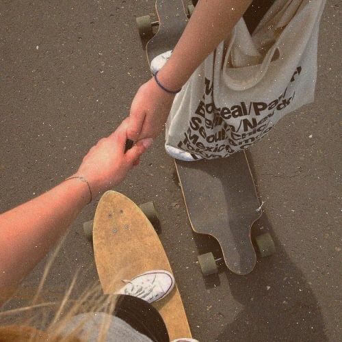 two people holding hands while standing next to skateboards on the ground with one person touching another's hand