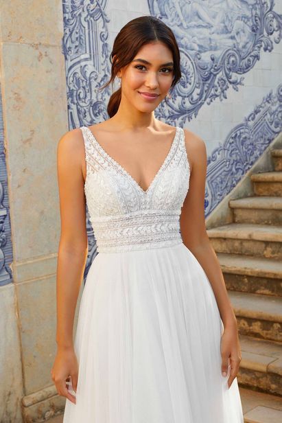 a woman standing in front of a blue and white wall wearing a wedding dress with an open back