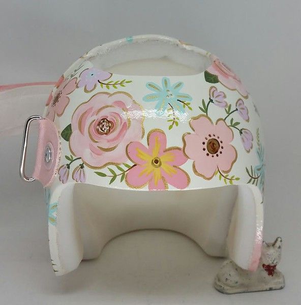 a white and pink helmet with flowers painted on the side, sitting in front of a white background