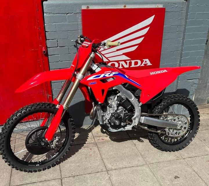 a red dirt bike parked in front of a honda logo on a brick wall next to a building