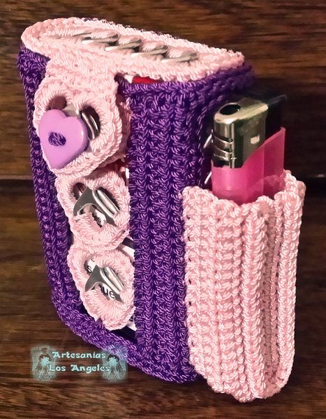 a pink and purple crocheted purse with two lighter holders in the center on a wooden surface