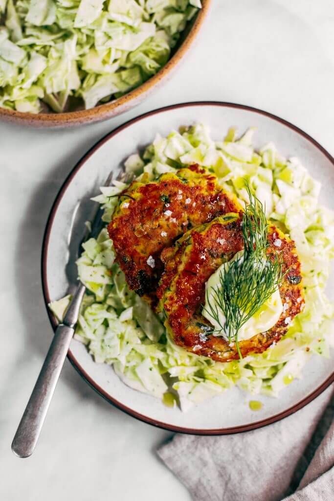 two plates filled with meat and vegetables next to a bowl of coleslaw on a table