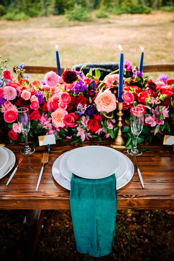 a wooden table topped with plates and glasses filled with pink, red and purple flowers