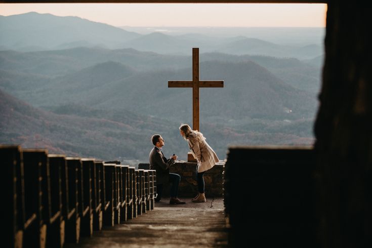 two people sitting at the top of a hill near a cross