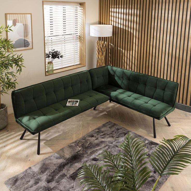 a green couch sitting on top of a wooden floor next to a plant in a living room