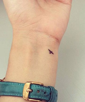 a woman's wrist with a small bird tattoo on the left side of her arm