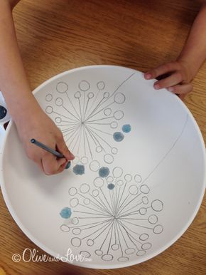 a person is drawing on a plate with blue circles and black markeres, while another hand holds a pen