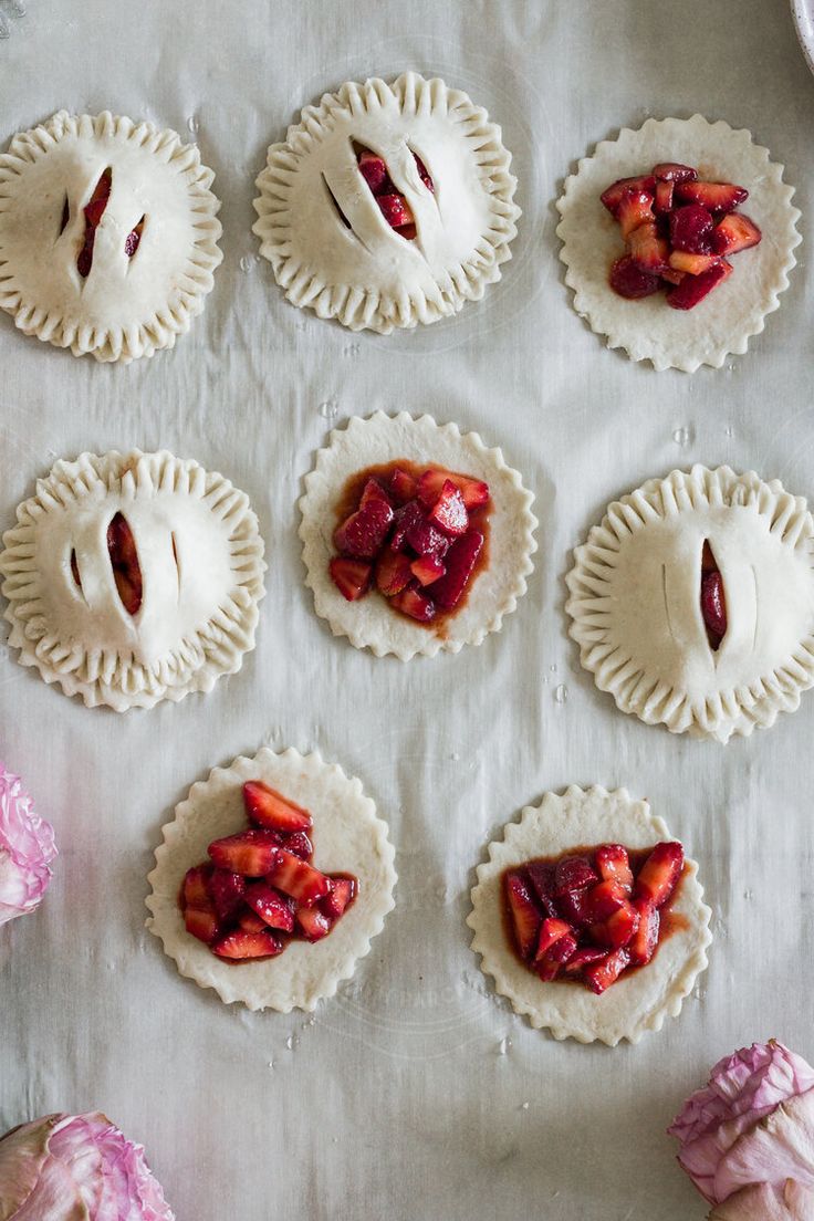 several pies with strawberries on them sitting on a table next to some pink flowers