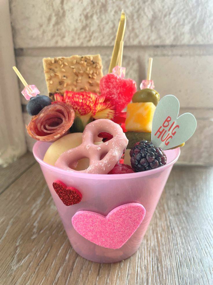 a pink cup filled with assorted donuts and other food on top of a wooden table