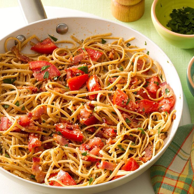 a pan filled with spaghetti and tomatoes on top of a table next to other dishes