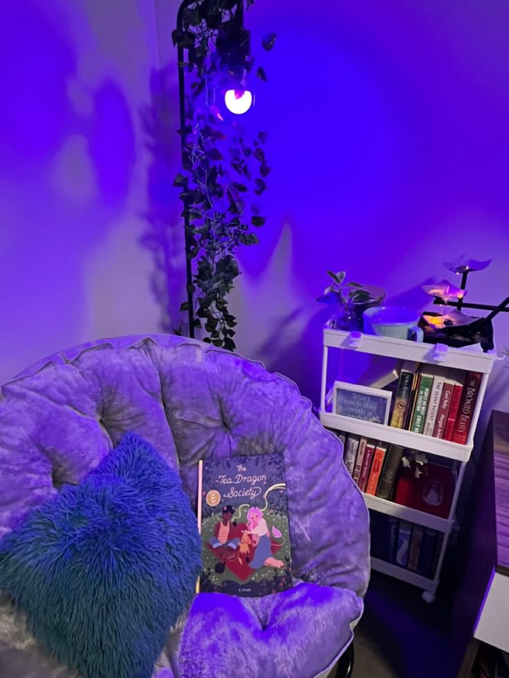 a purple chair sitting in front of a book shelf filled with books and a pillow