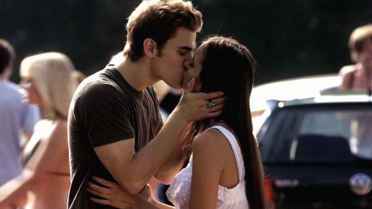 a man kissing a woman on the cheek in front of parked cars and people walking around