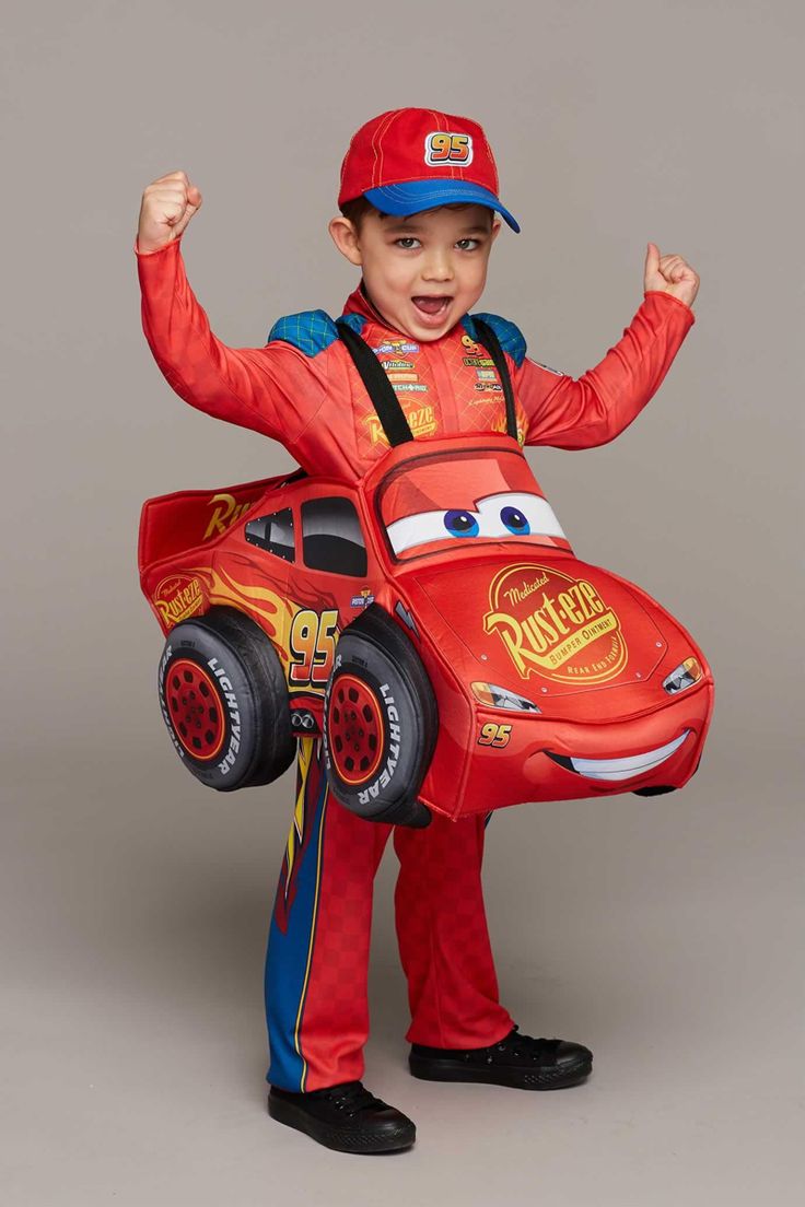 a young boy in a red shirt and blue hat is holding a car shaped cardboard box