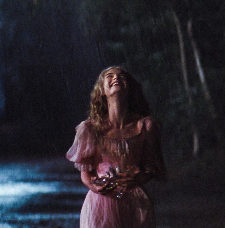 a woman standing in the rain with her eyes closed and holding an umbrella over her head