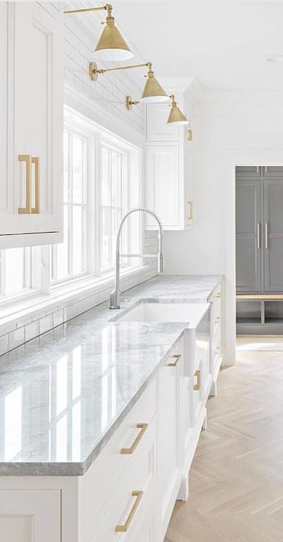 a white kitchen with marble counter tops and gold pulls on the cabinet doors is pictured in this image