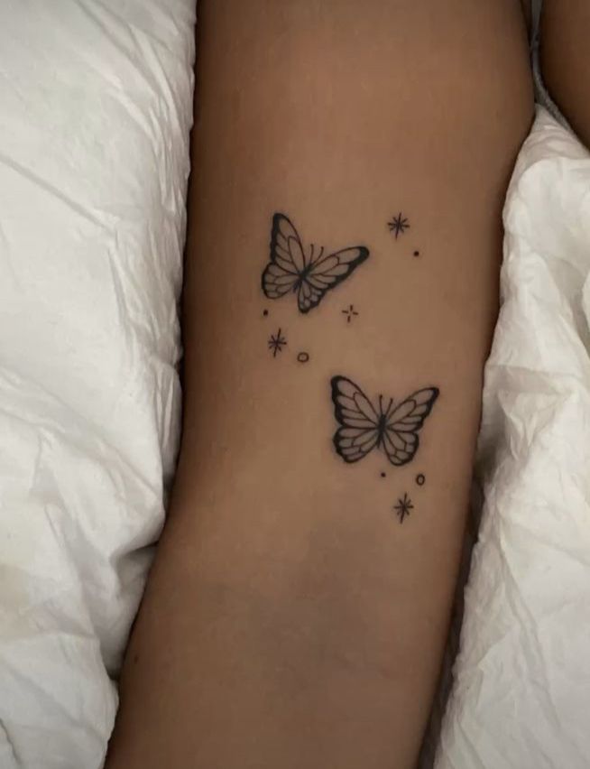 two butterflies flying in the air on a woman's left arm with stars around it