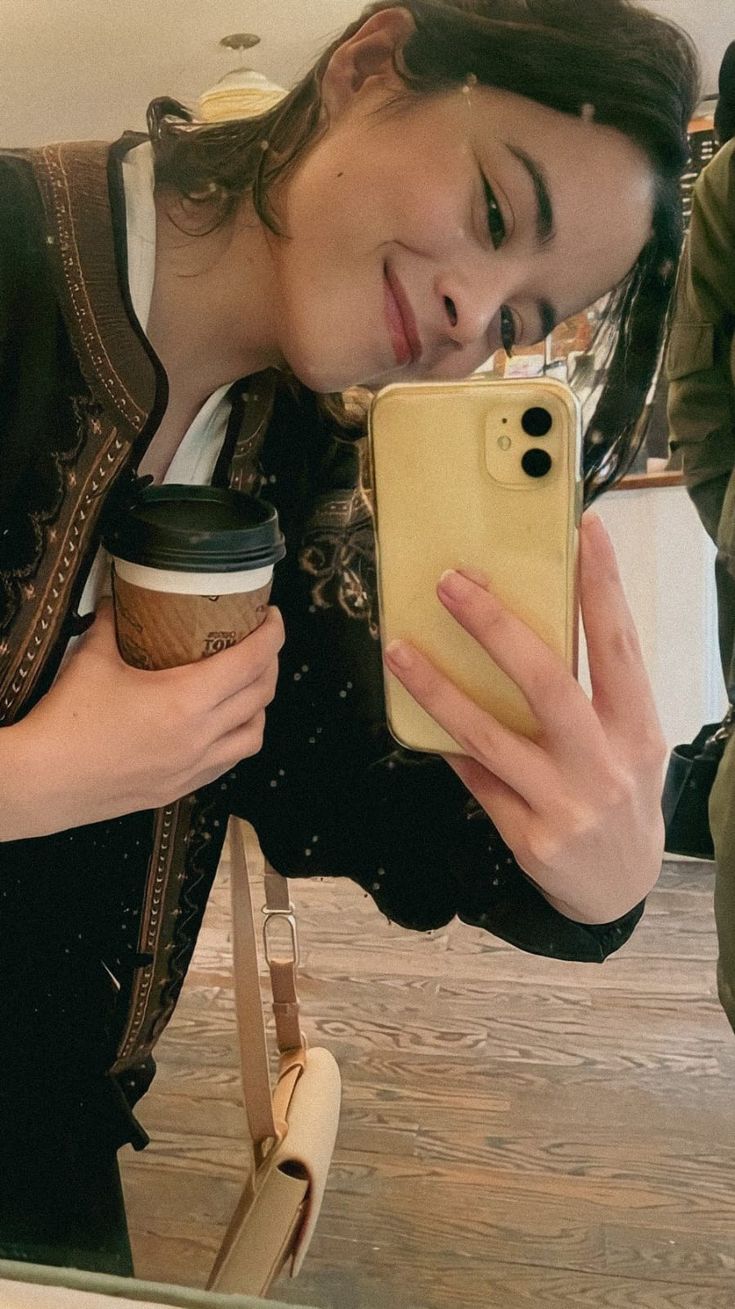 a woman taking a selfie with her cell phone and holding a cup of coffee