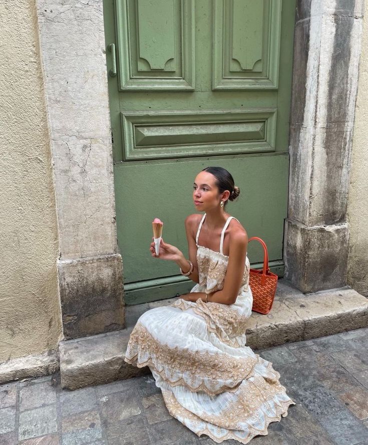 a woman sitting on the ground in front of a green door holding an ice cream cone