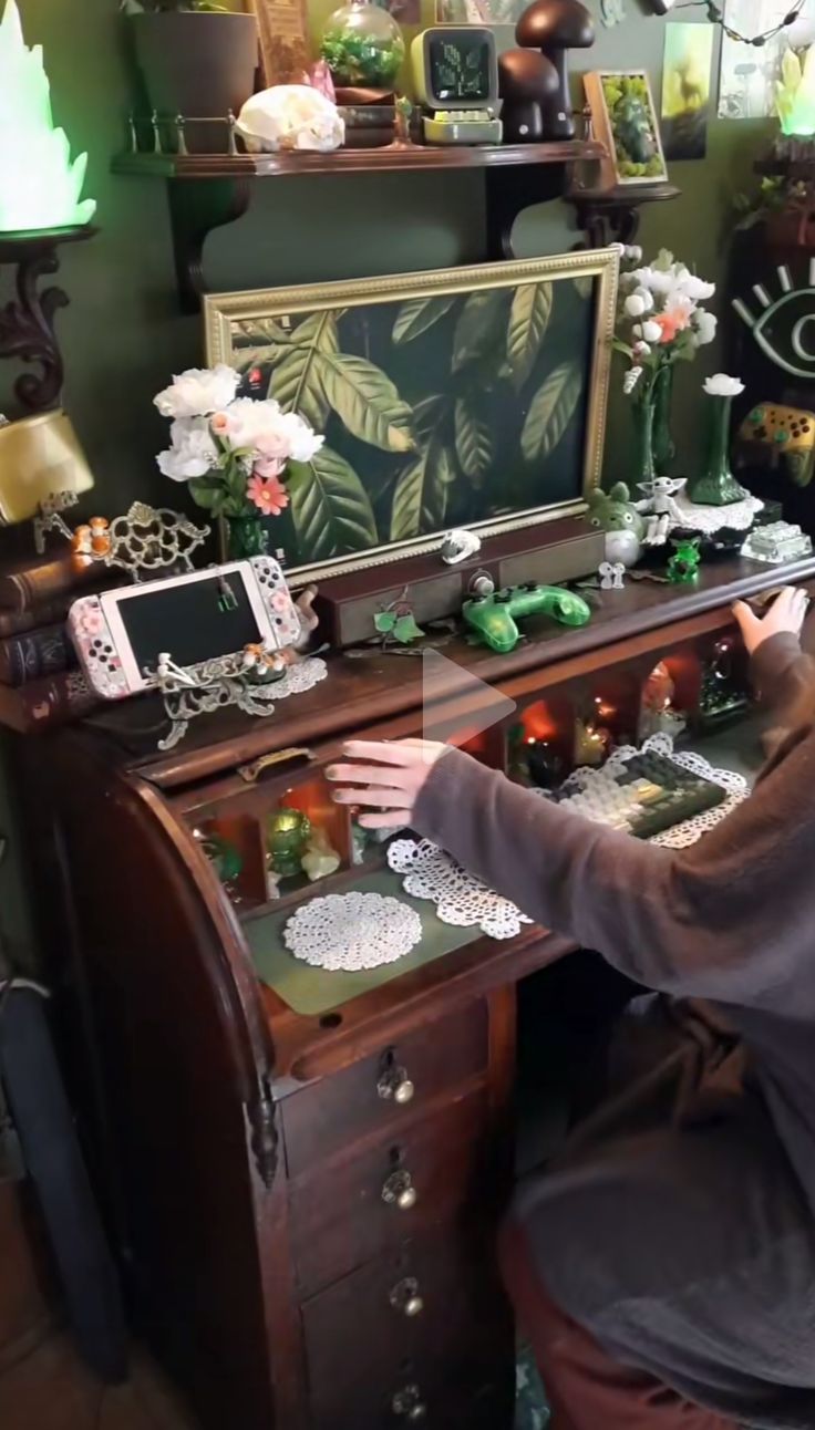 a woman sitting at a desk with lots of decorations on top of it and holding her hand out to the camera