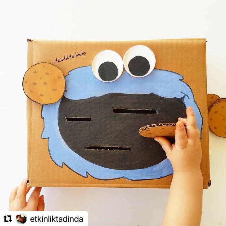 a child's hand is holding a cardboard cutout of an cookie monster with googly eyes