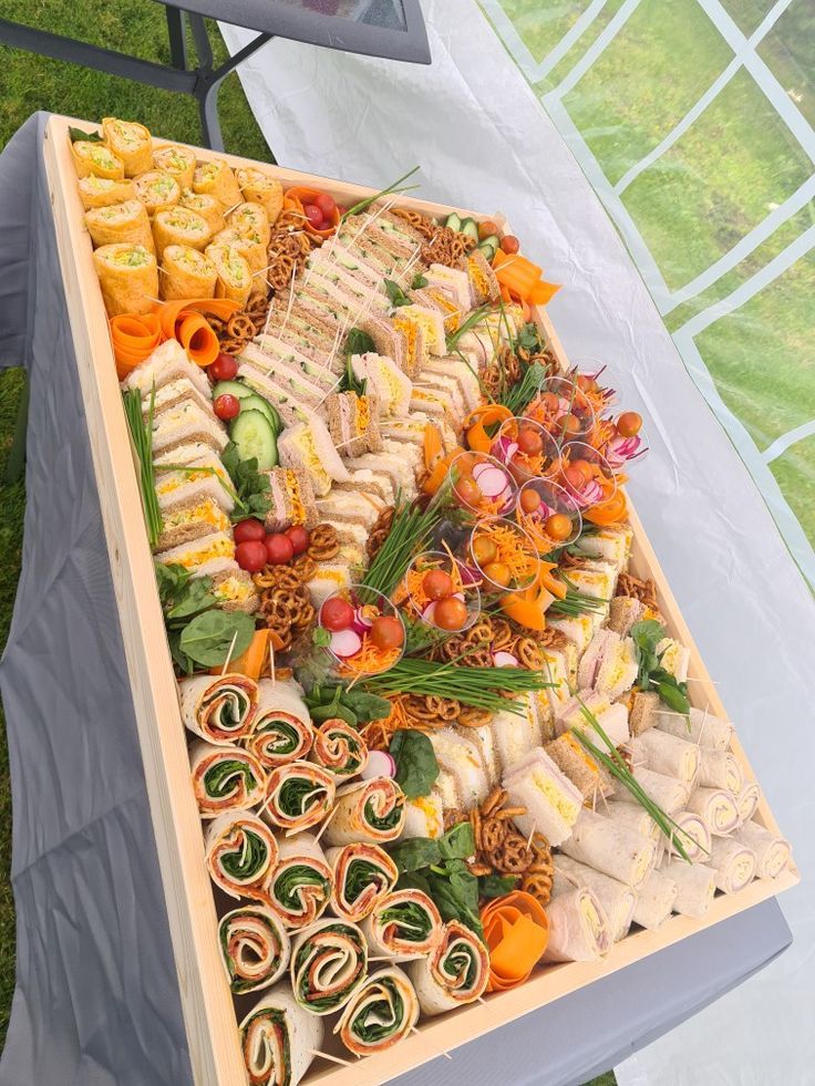 an assortment of food is displayed in a wooden tray on a table outside with grass