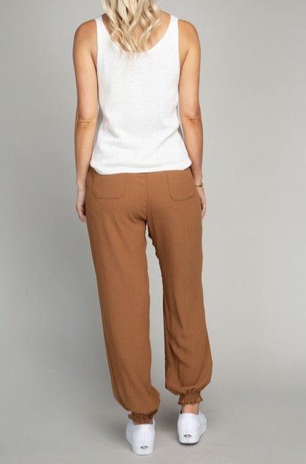 Designed for all-day comfort, these Brown Jogger Pants are crafted from a lightweight crinkle-textured fabric with no stretch. An elastic waistband and string drawstring at the waist provide a secure fit, while smocking at the ankle cuffs offers a flexible fit. Two side pockets in the front and two pockets in the back make it easy to store your small essentials. Brown Ankle-length Pants With Elastic Waistband, Brown Trousers With Elastic Waistband, Brown Tapered Leg Pants For Loungewear, Brown Tapered Leg Loungewear Pants, Casual Brown Tapered Leg Pants For Loungewear, Brown Straight Pants With Elastic Waistband, Brown Bottoms With Elastic Waistband And Loosely Fitted Hips, Loosely Fitted Brown Bottoms With Elastic Waistband, Relaxed Brown Bottoms For Loungewear