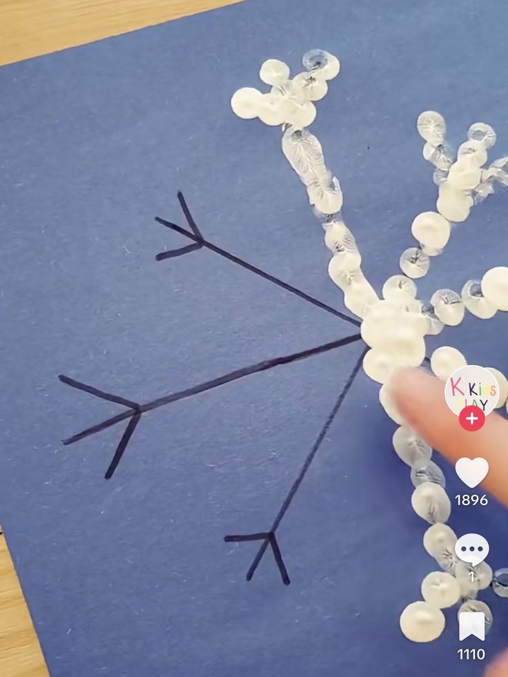 someone is making a snowflake out of buttons and plastic beads on a piece of blue paper