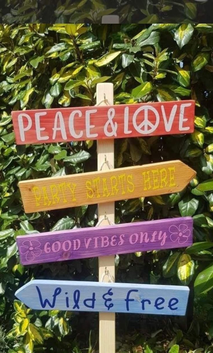 a wooden sign that says peace and love with other signs on it in front of some bushes