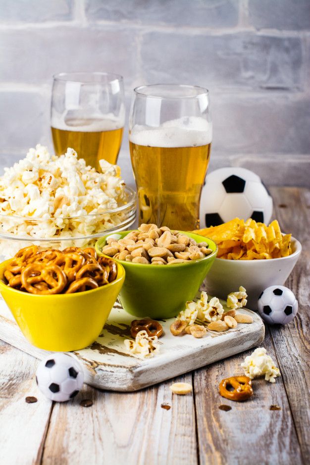 a table topped with bowls filled with food next to two beer glasses and soccer balls