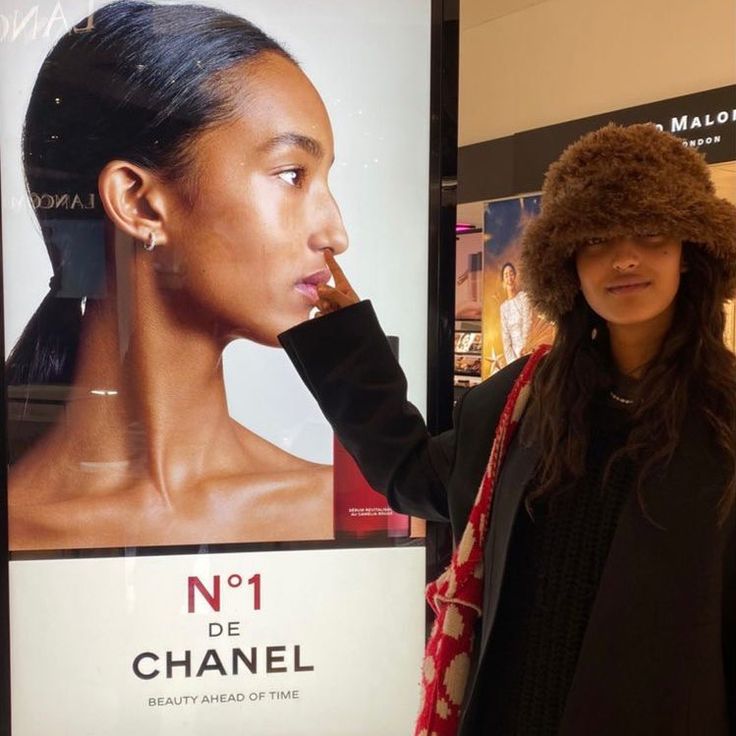 a woman standing next to a poster with a fur hat on top of her head