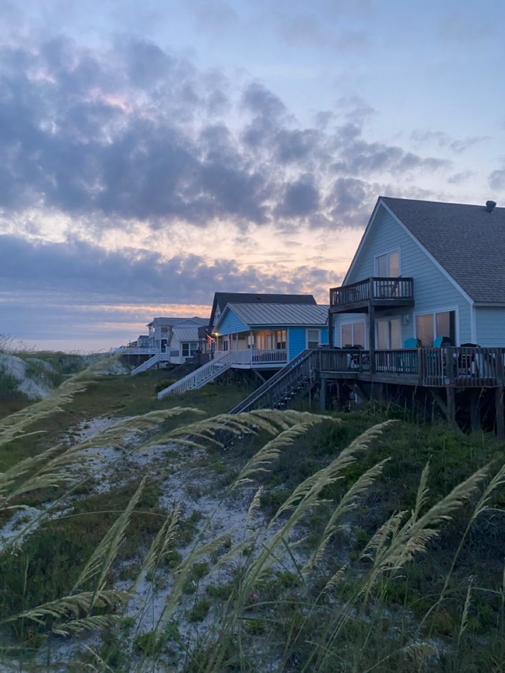 a house on the beach at sunset with grass in front and stairs leading to it