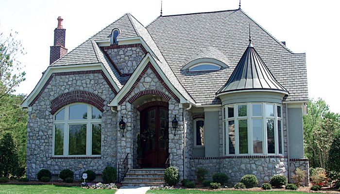 a stone house with arched windows and a walkway leading to the front door on a sunny day