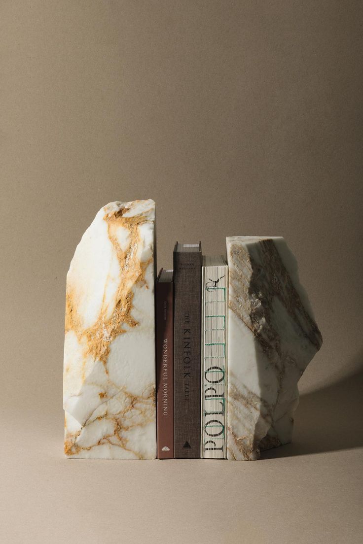 two books are stacked on top of each other in front of a gray background, with the bookends made out of marble