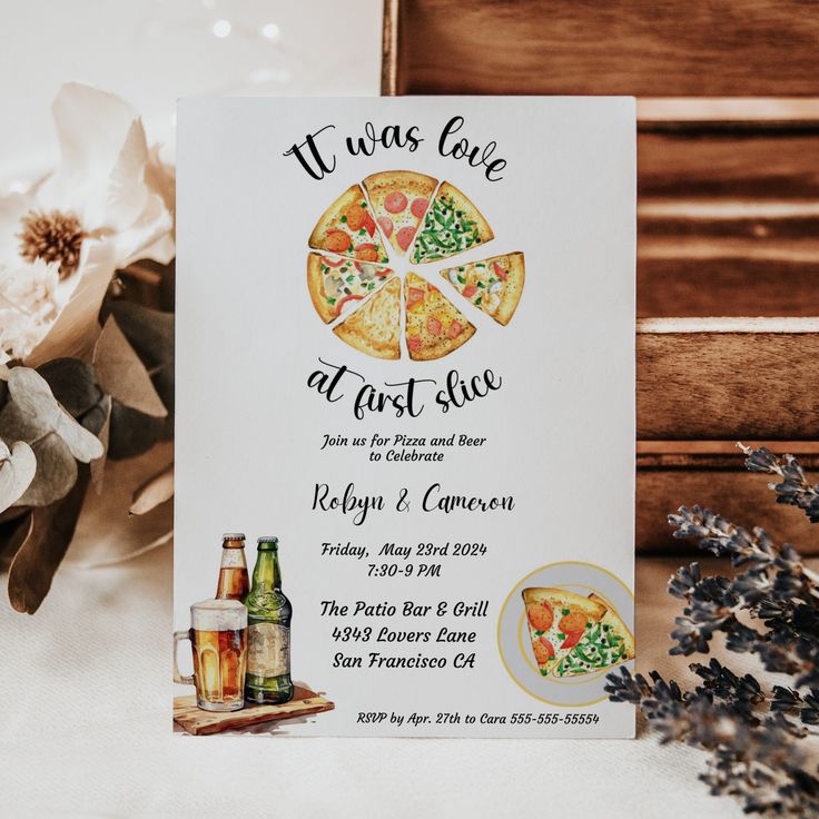 a pizza themed wedding card on a table next to some flowers and wine bottles with the words, it was love at first slice