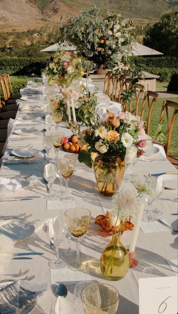 a long table is set up with wine glasses and flowers in vases on it