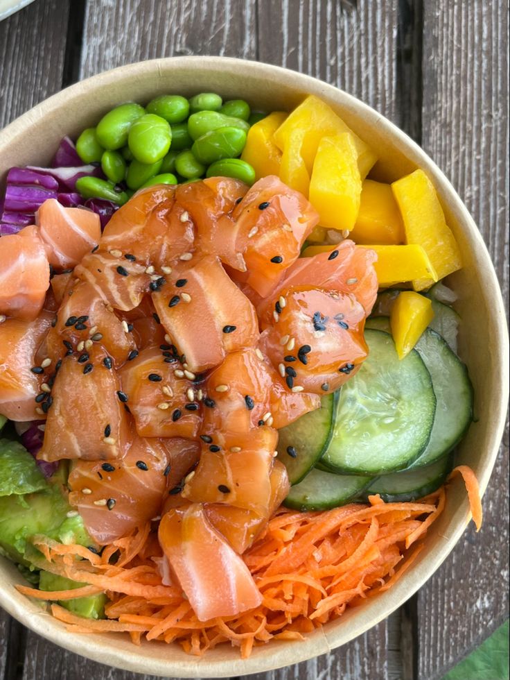 a bowl filled with salmon, cucumbers, carrots, and green beans