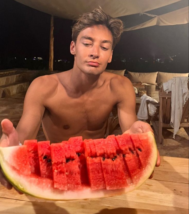 a man sitting at a table with a slice of watermelon in front of him