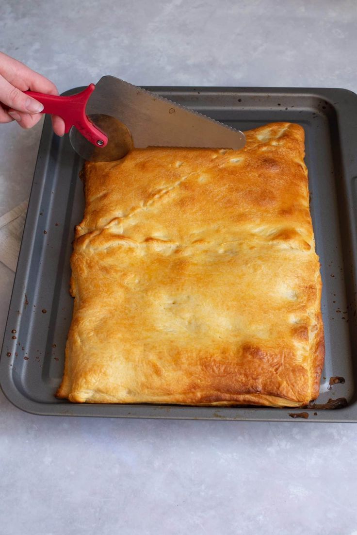 a person cutting up food on top of a pan with a red handled spatula