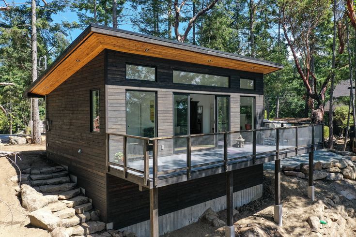 a small house sitting on top of a sandy beach next to trees and rocks in front of it