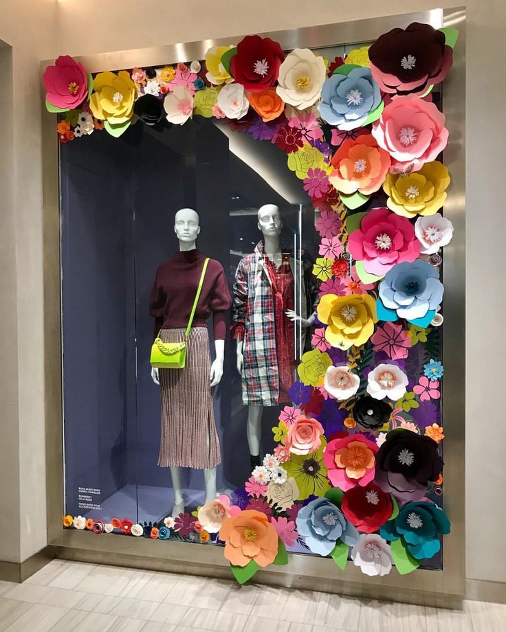 a window display with paper flowers on the front and back of it, featuring mannequins dressed in colorful clothing