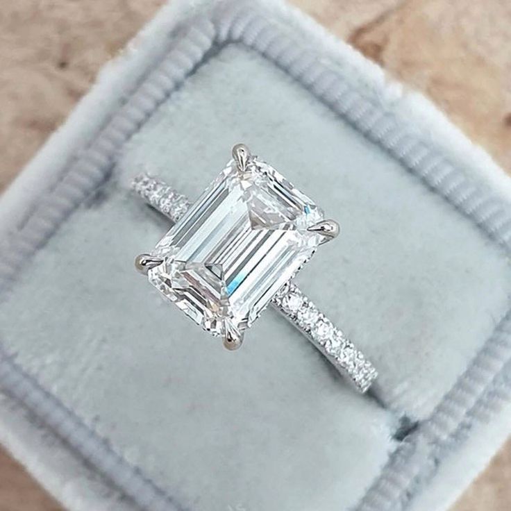 an emerald - cut diamond ring sits in a velvet box on top of a carpeted surface