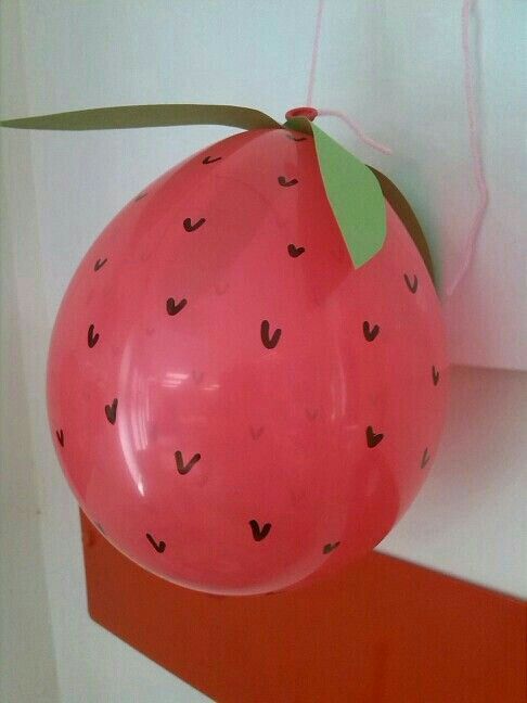 a balloon shaped like a strawberry hanging from a wall with a ribbon attached to it