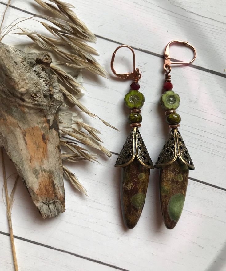 Beautiful mottled Olive green stones cloaked in a brass filigree Cone dangle underneath  a Czech glass flower and Garnet rondelle. This one of a kind pair measures 2-1/2 inches long. Brass and copper findings with Copper ear wires. Artisan Green Copper Jewelry, Bohemian Green Earrings With Natural Stones, Handmade Bronze Czech Glass Earrings, Handmade Bronze Jewelry With Czech Glass, Handmade Czech Glass Bronze Jewelry, Bohemian Jade Jewelry, Bohemian Green Copper Jewelry, Vintage Green Copper Jewelry, Handmade Brown Jade Jewelry