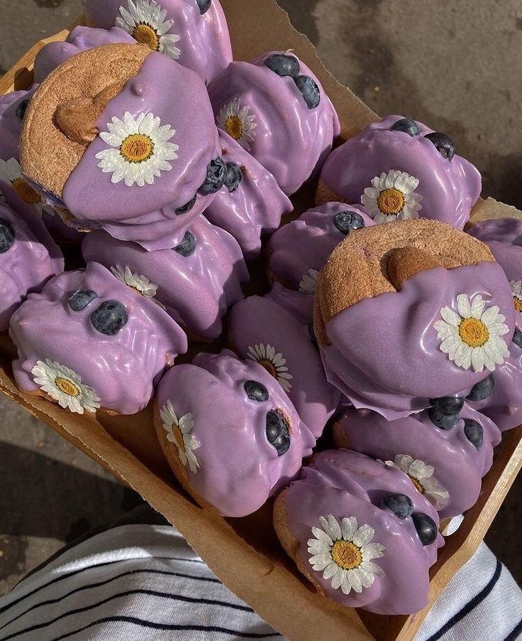 a box filled with purple frosted donuts covered in blueberries and daisies