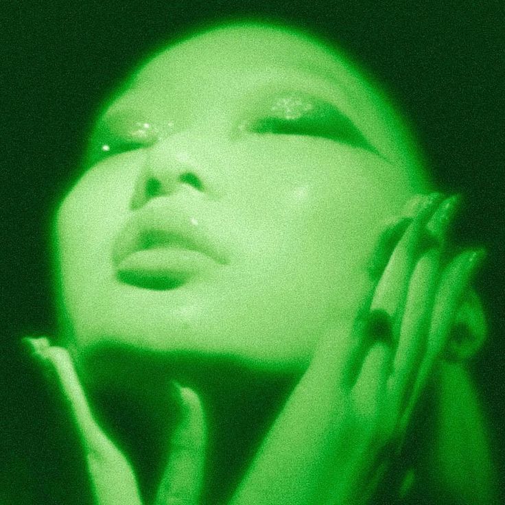 a woman with her eyes closed and hands on her face, in the green light